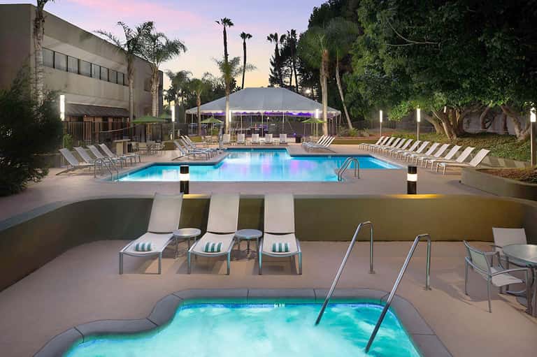 Resort pool at dusk with tent pavilion, lounge chairs, palm trees, and illuminated spa area