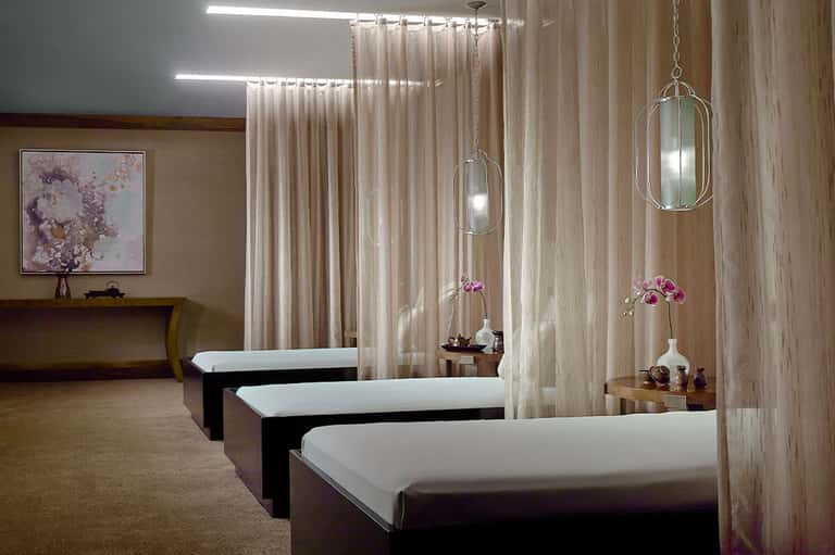 Spa treatment room with massage beds, hanging pendant lights, and pink orchid flowers