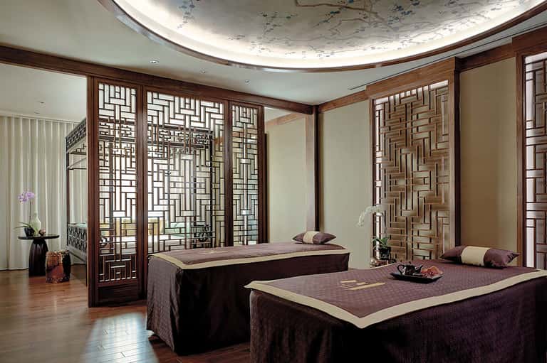Luxury spa treatment room with twin massage beds and decorative wood screens