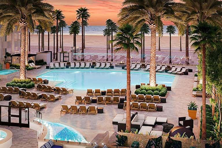Beachfront resort pool at sunset with palm trees, lounge chairs, and ocean view