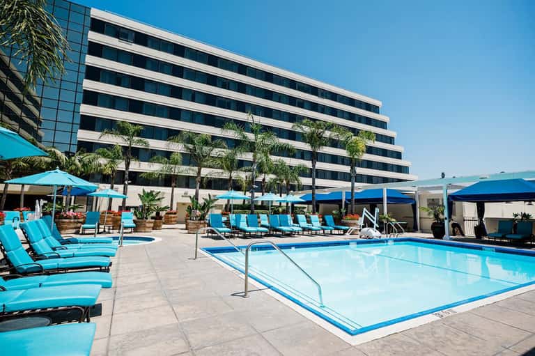 Modern resort pool deck with turquoise umbrellas, lounge chairs, and high-rise building