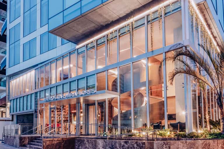 Modern restaurant with floor-to-ceiling windows, palm tree decor, and ambient evening lighting