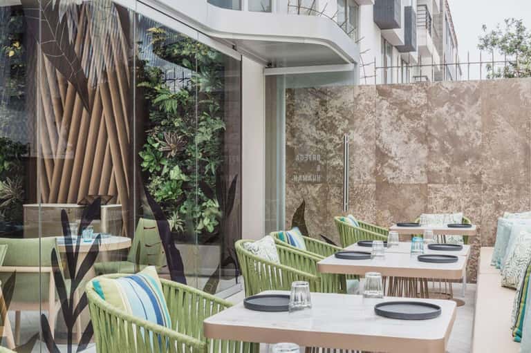 Modern restaurant terrace with green rope chairs, white tables, and living plant wall backdrop