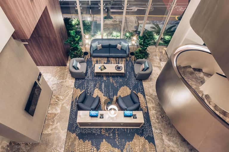 Contemporary hotel lobby with gray seating, large windows, plants, and circular elements