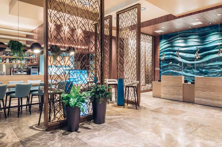 Modern hotel lobby with geometric wood screens, bar seating, and ocean artwork