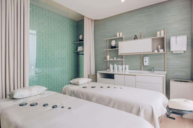 Spa treatment room with twin massage beds and green tile shower area with modern amenities