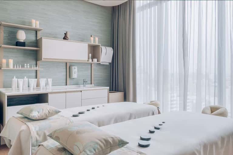Modern spa treatment room with twin beds, mint green walls, white storage, and ocean view