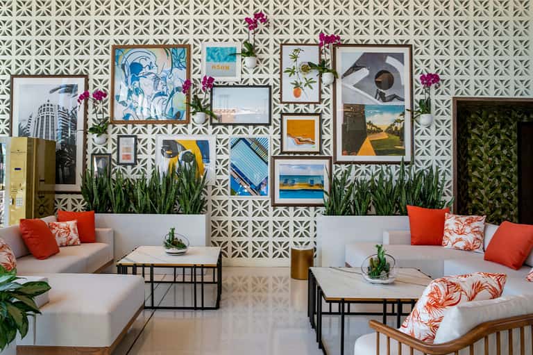 Modern lobby lounge with geometric patterned wallpaper, gallery wall of framed photos, and orange accent pillows