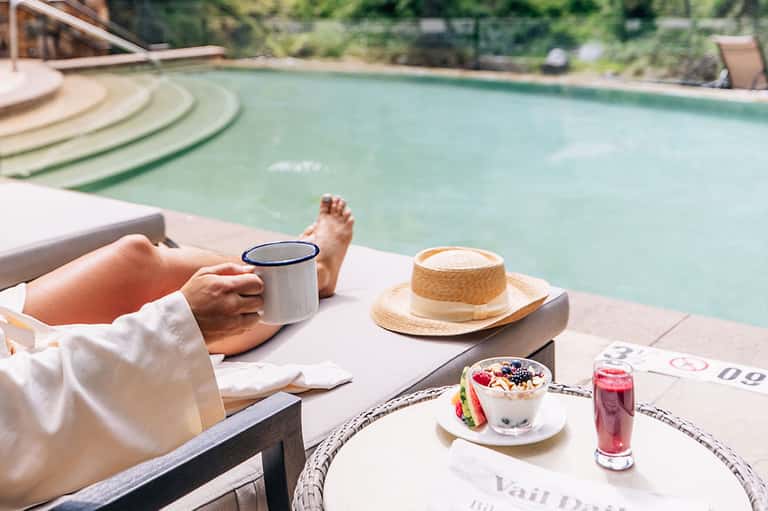 Poolside relaxation with coffee mug, straw hat, and appetizer on white cushioned lounger