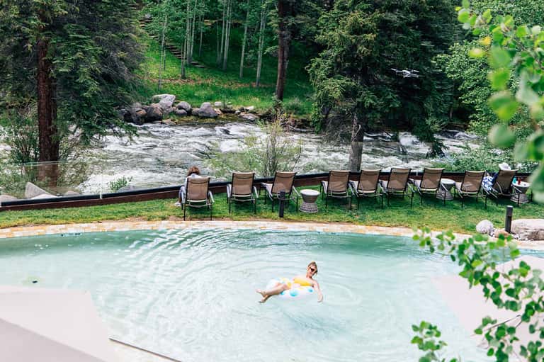 Natural hot spring pool surrounded by forest, river, and lounge chairs