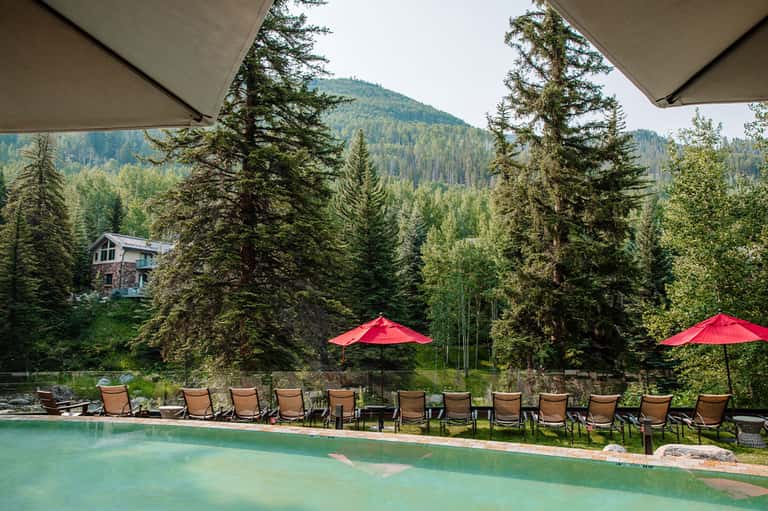 Scenic mountain resort pool with red umbrellas, turquoise water, and forest backdrop