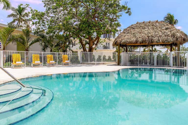 Resort pool with turquoise water, yellow lounge chairs, and thatched shelter structure