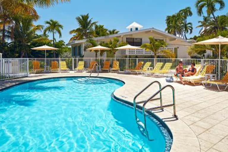 Resort pool surrounded by white railings, yellow lounge chairs, and palm tree landscaping