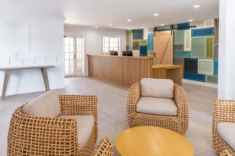 Bright hotel lobby with woven wicker chairs, colorful louvered wall panels, and wooden reception desk