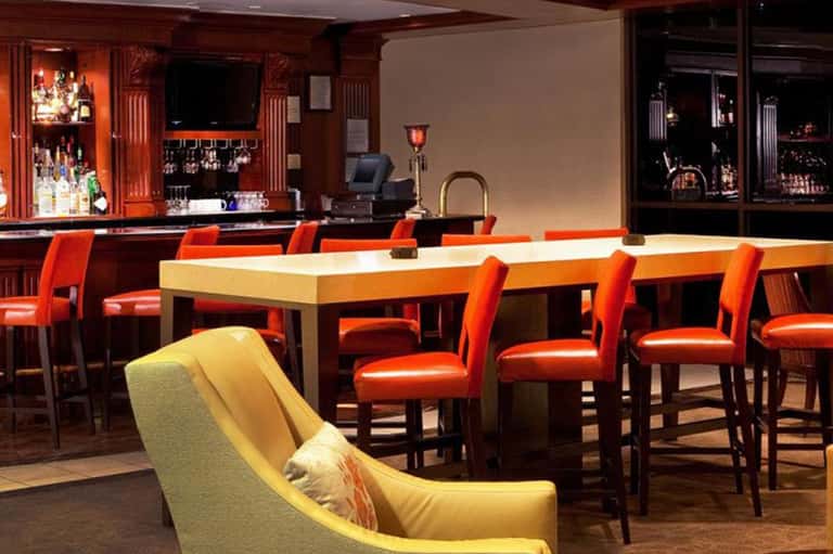 Modern lounge bar with orange chairs, cream counters, and wood-paneled back bar