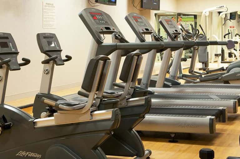 Fitness center with rows of exercise bikes and cardio equipment along white wall