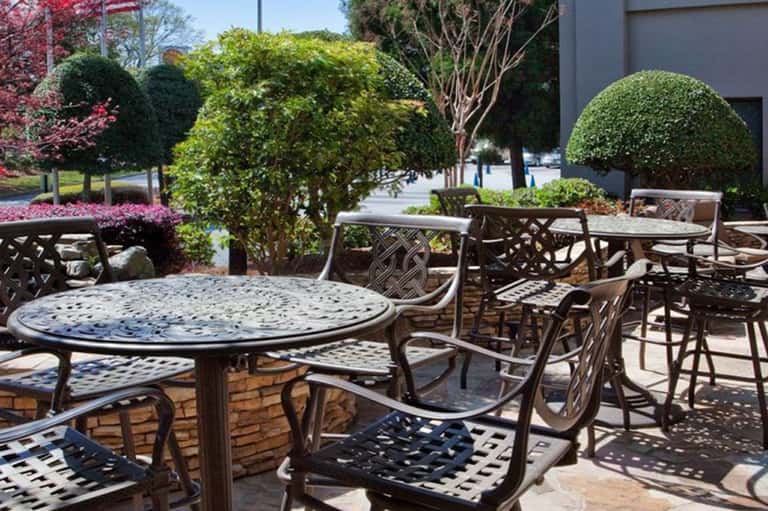 Outdoor patio seating with round tables, metal chairs, and manicured landscaping