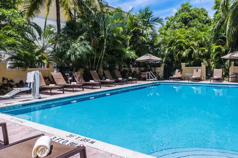 Resort swimming pool with diving board, lounge chairs, tropical palms, and tiki umbrellas