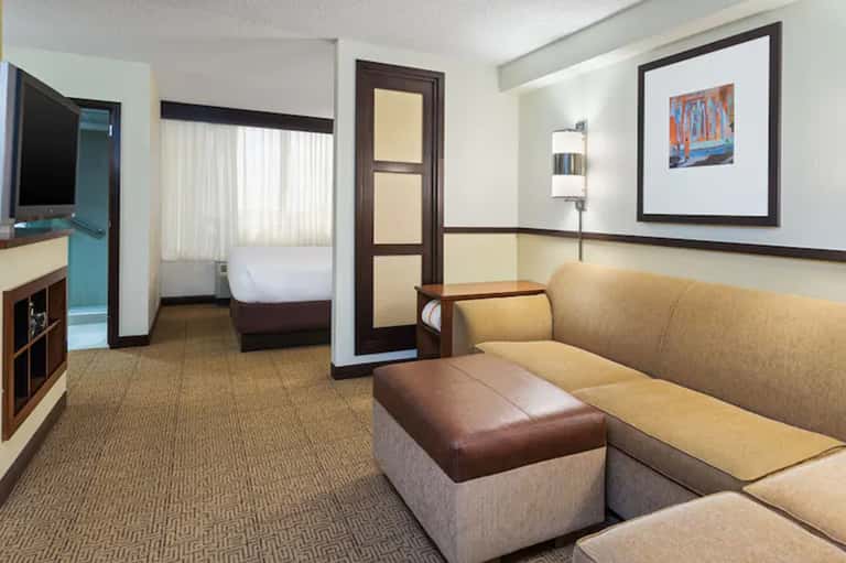 Hotel suite interior with beige sofa, queen bed, flat-screen TV, and contemporary furnishings