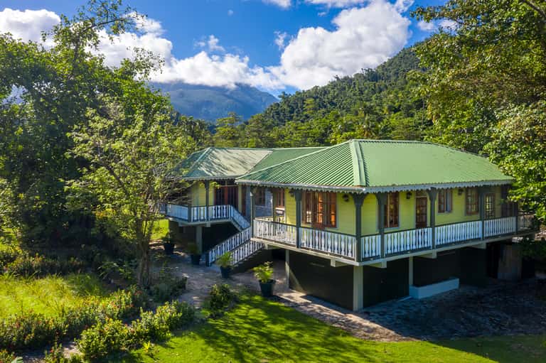 Colorful cottage with yellow walls, green roof, and blue railings nestled in lush mountain forest