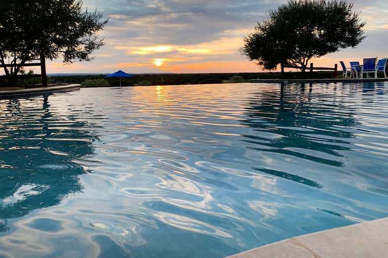 Resort infinity pool at sunset reflecting golden sky with lounge chairs and ocean horizon view