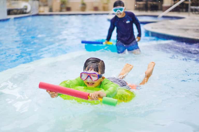 Child in neon green swimsuit learning to swim with instructor in shallow pool
