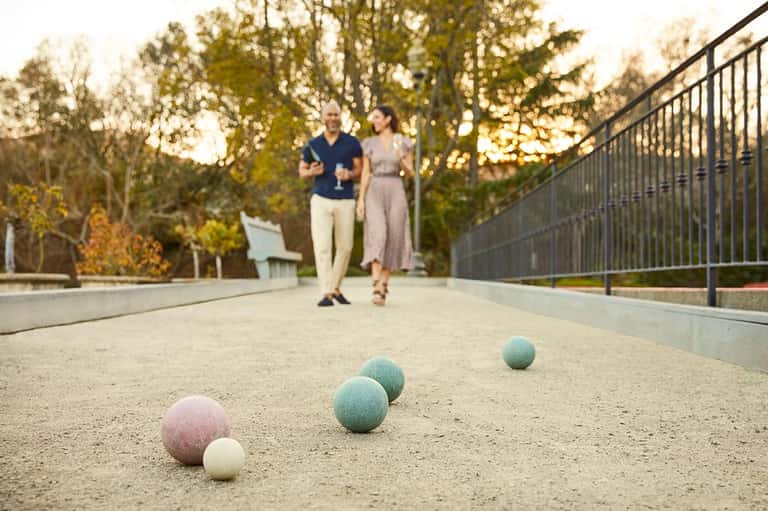 Bocce ball court with colored balls in foreground and couple jogging in background