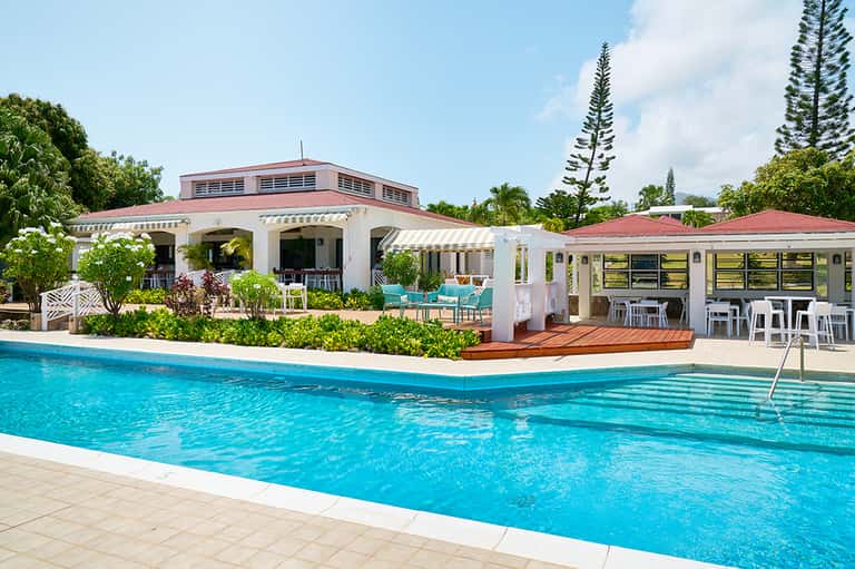 Resort pool facility with white main building, turquoise water, and tropical vegetation