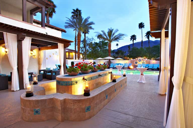 Luxury resort courtyard at dusk with illuminated curved stone features, cabanas, and pool with mountain backdrop