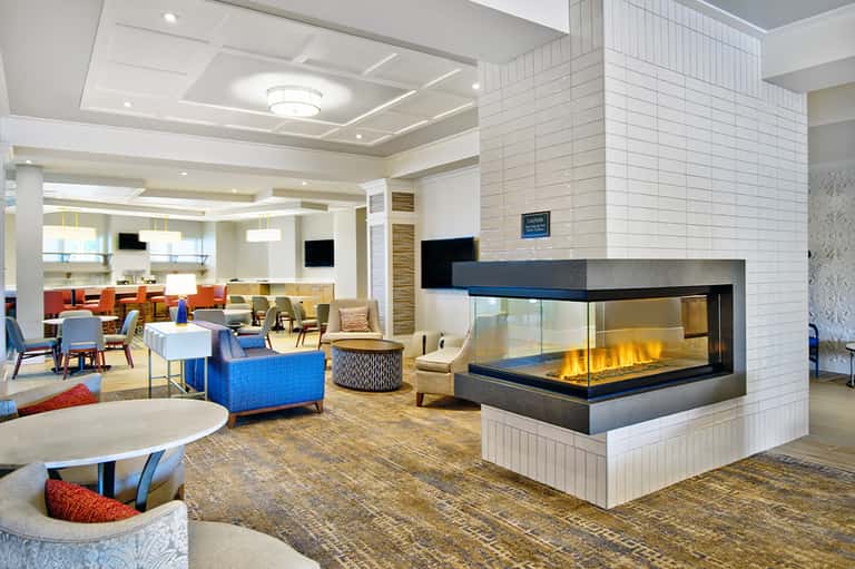 Contemporary hotel lobby with fireplace, colorful seating, coffered ceiling, and modern furnishings
