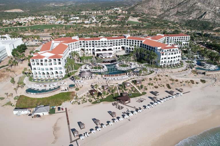 Aerial view of large beachfront resort complex with red roofs and mountain backdrop
