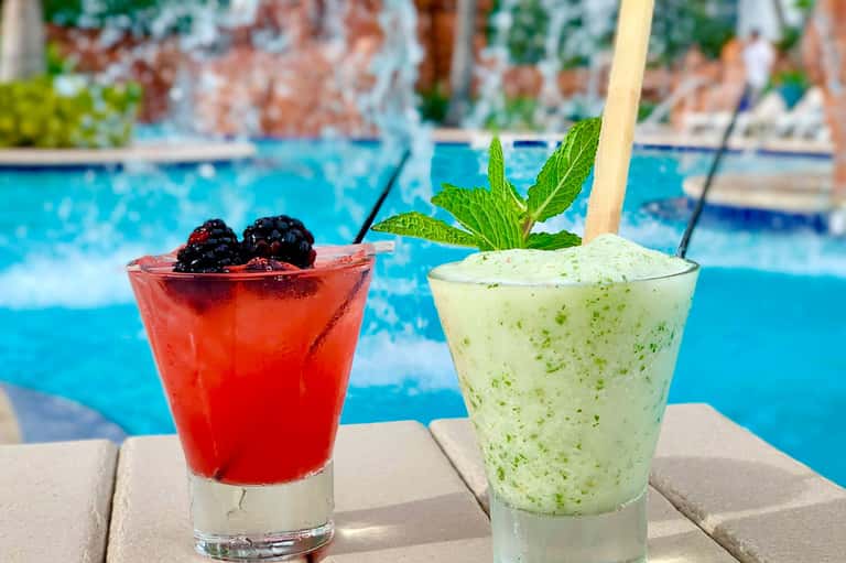 Two colorful cocktails by poolside: red berry drink and green mint mojito with straws