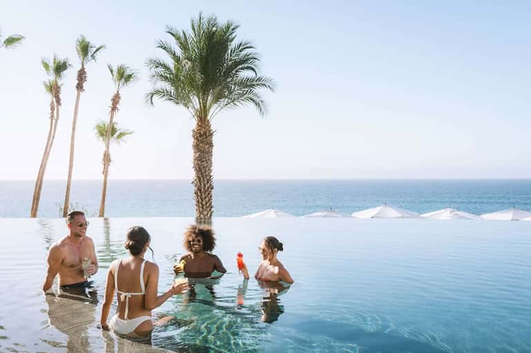Guests swimming in infinity pool with palm trees and ocean horizon backdrop