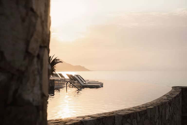 Serene waterfront deck with lounge chairs, calm sea, and golden hour sunrise lighting