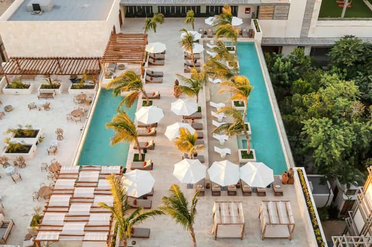 Aerial view of modern resort with multiple pools, white umbrellas, and palm trees