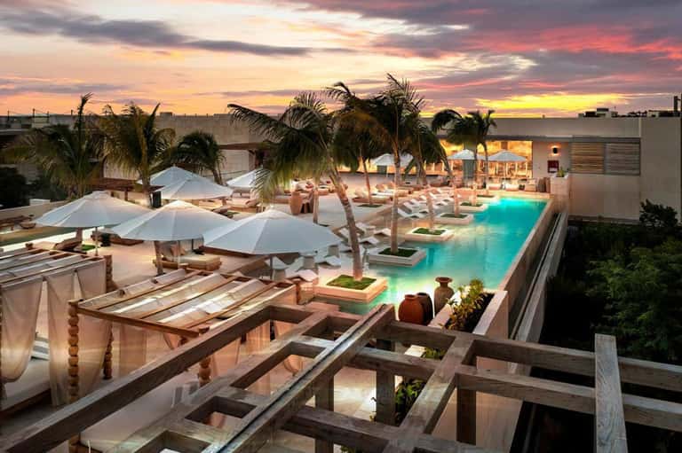 Beachfront resort pool illuminated at dusk with umbrellas and palm trees
