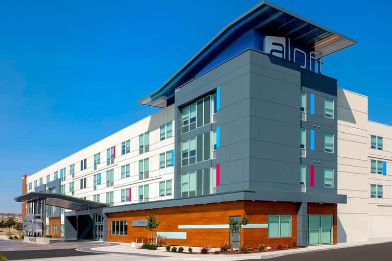 Modern Aloft hotel exterior with blue and orange accents against clear sky
