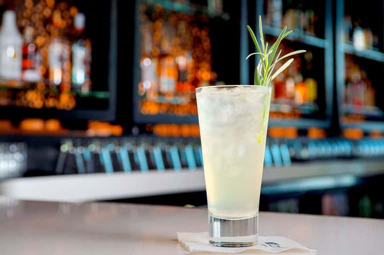 Refreshing cocktail with herb garnish at modern bar with liquor bottles