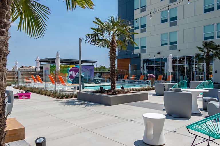 Modern poolside deck with colorful lounge chairs, white umbrellas, and contemporary building