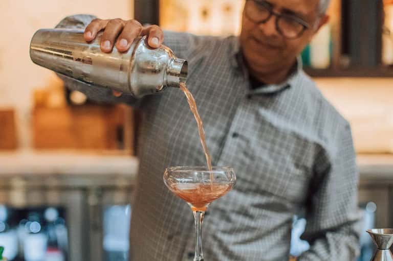 Bartender pouring amber cocktail from shaker into coupe glass at hotel bar