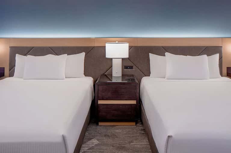 Upscale hotel room with two queen beds, dark headboards, and modern bedding