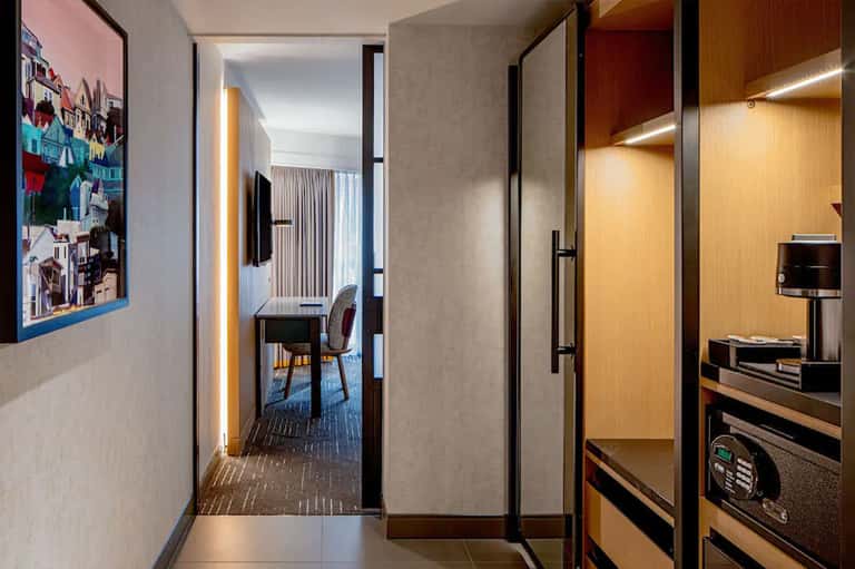 Modern hotel room corridor with wood paneling, desk workspace, and entertainment area