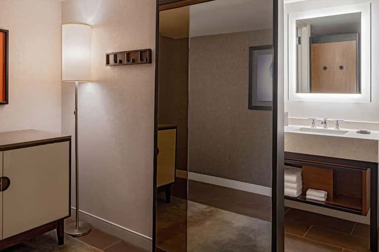 Modern hotel bathroom with marble sink, walk-in shower, and taupe finishes