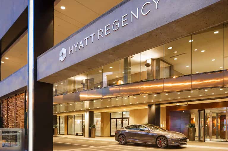 Hyatt Regency hotel entrance at night with illuminated signage and luxury car parked outside