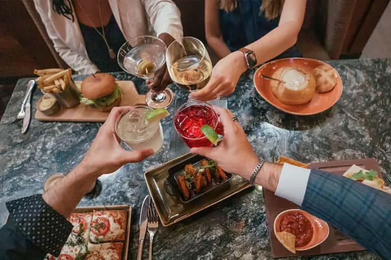 Overhead shot of people cheering with cocktails and appetizers at dining table