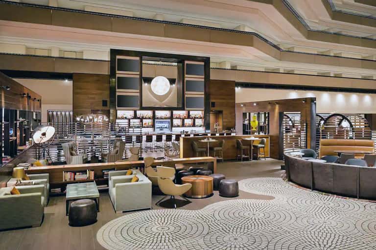 Contemporary hotel lobby with modern bar, geometric patterned carpet, and brown wood accents