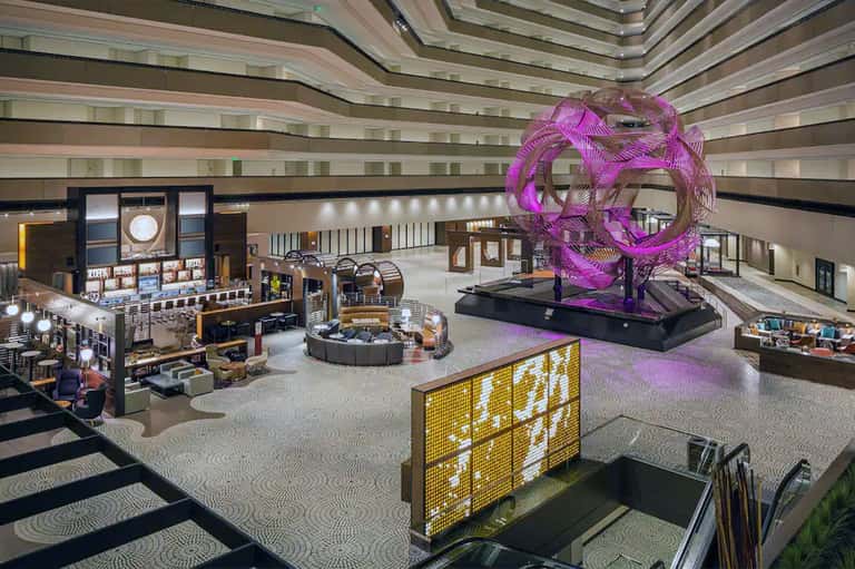 Modern hotel lobby atrium with multi-level architecture, shops, and purple sculptural art installation