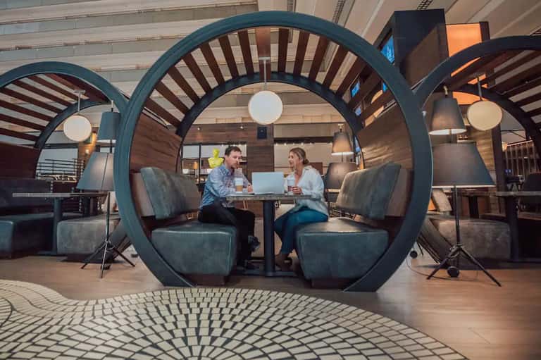 Contemporary lounge with large circular teal accent structure seating two people, pendant lights, and wooden flooring