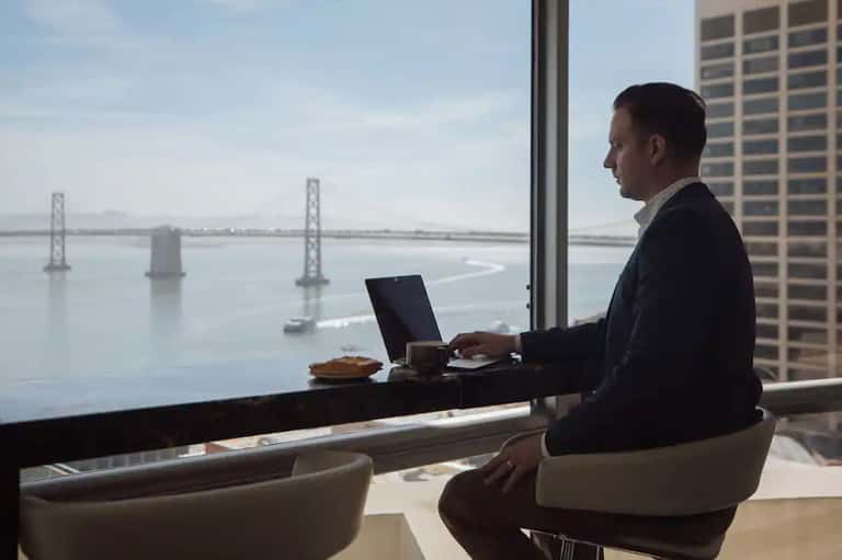 Man working on laptop at high-rise office desk with bay bridge city view