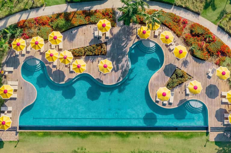 Aerial view of resort pool with curved turquoise water, yellow umbrellas, and wooden decking